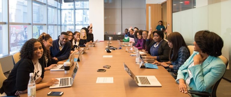 Imagem de pessoas de etnias diversas em um escritório. Elas estão em uma sala de reuniões.