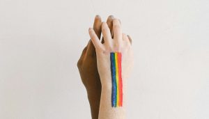 Imagem de duas mãos dadas em direção ao alto. Uma delas contém pintada a bandeira do orgulho LGBTQIAP+. A foto ilustra a nota sobre o Edital LGBT+ Orgulho.